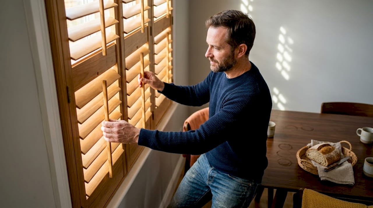 Een man doet de houten shutters in de eetkamer open.