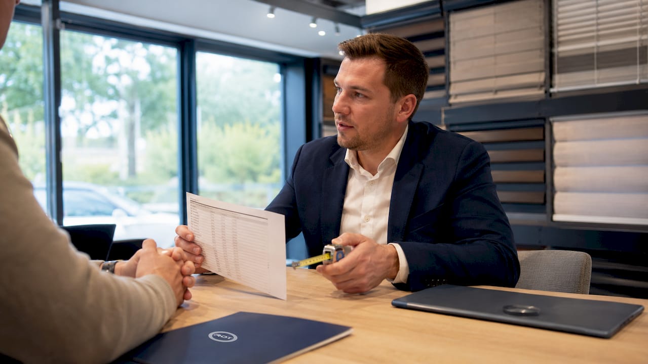 De verkoper legt uit welke factoren de prijs van shutters bepalen.