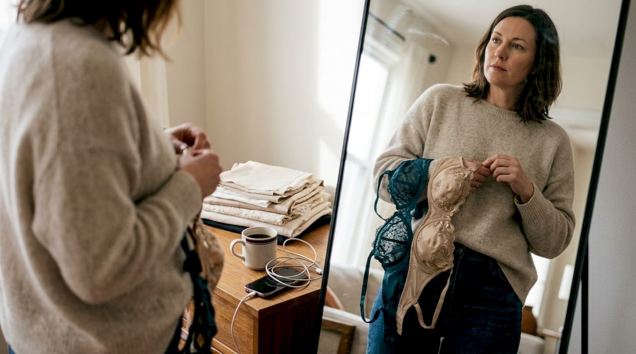 Une femme essaie différents ensembles de lingerie devant le miroir du salon, hésitant sur celui qui lui va le mieux.