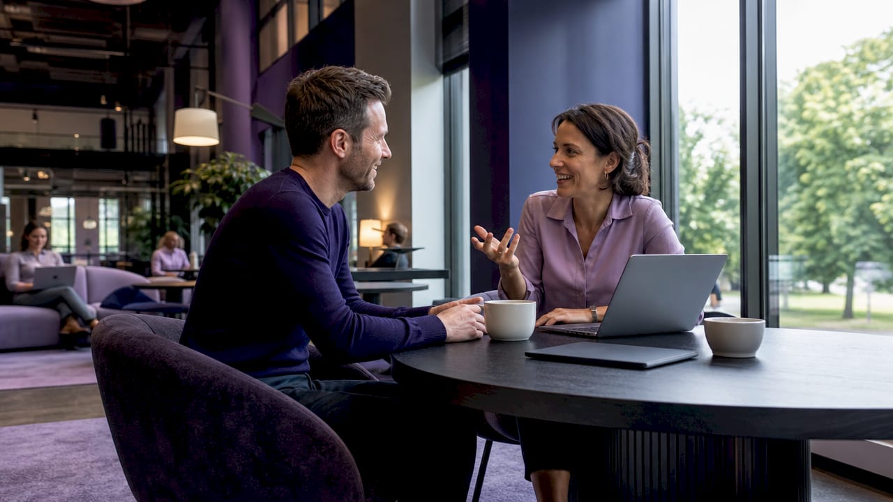 Två personer sitter och pratar tillsammans i en coworkinglokal.