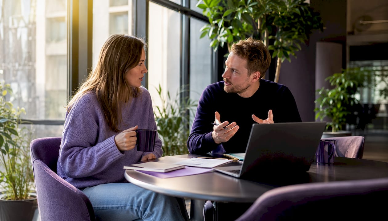 Två personer sitter och pratar vid ett flexibelt skrivbord på ett coworkingkontor.