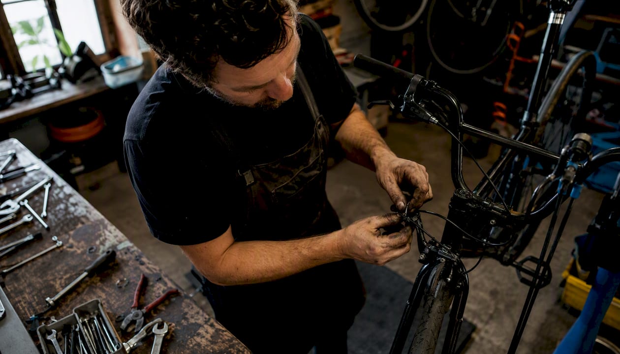 Un mécanicien cycle en train d’effectuer la révision des freins d’un vélo dans son atelier.