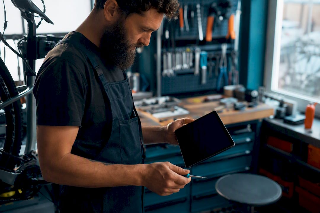 Un technicien en atelier travaille sur une pièce de vélo tout en consultant une tablette.