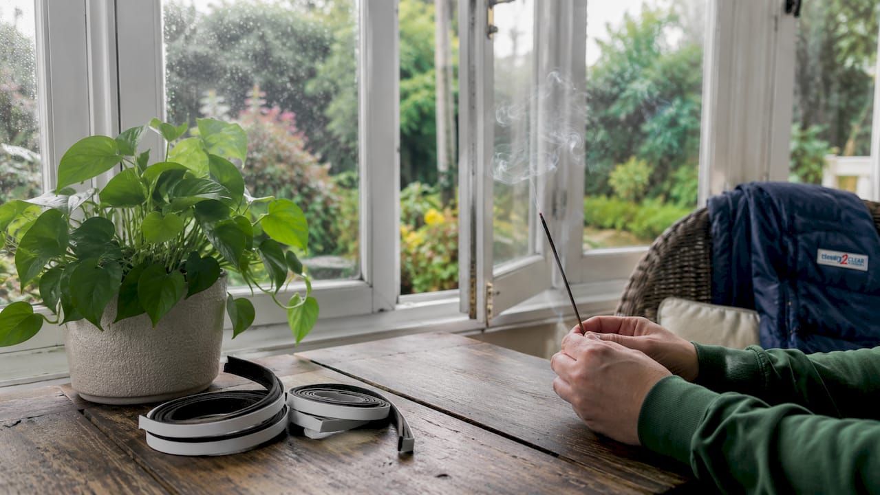 Hands checking window drafts with incense stick