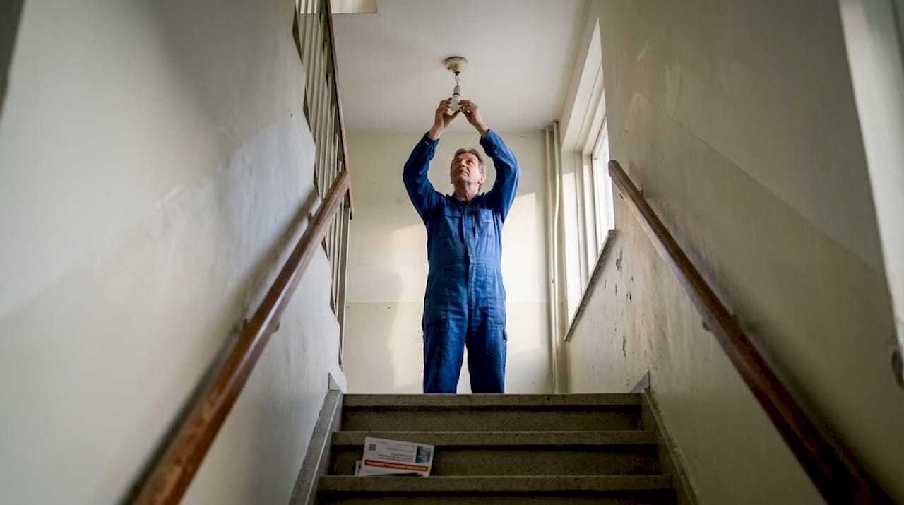 De huismeester vervangt een ledlamp in het trappenhuis.