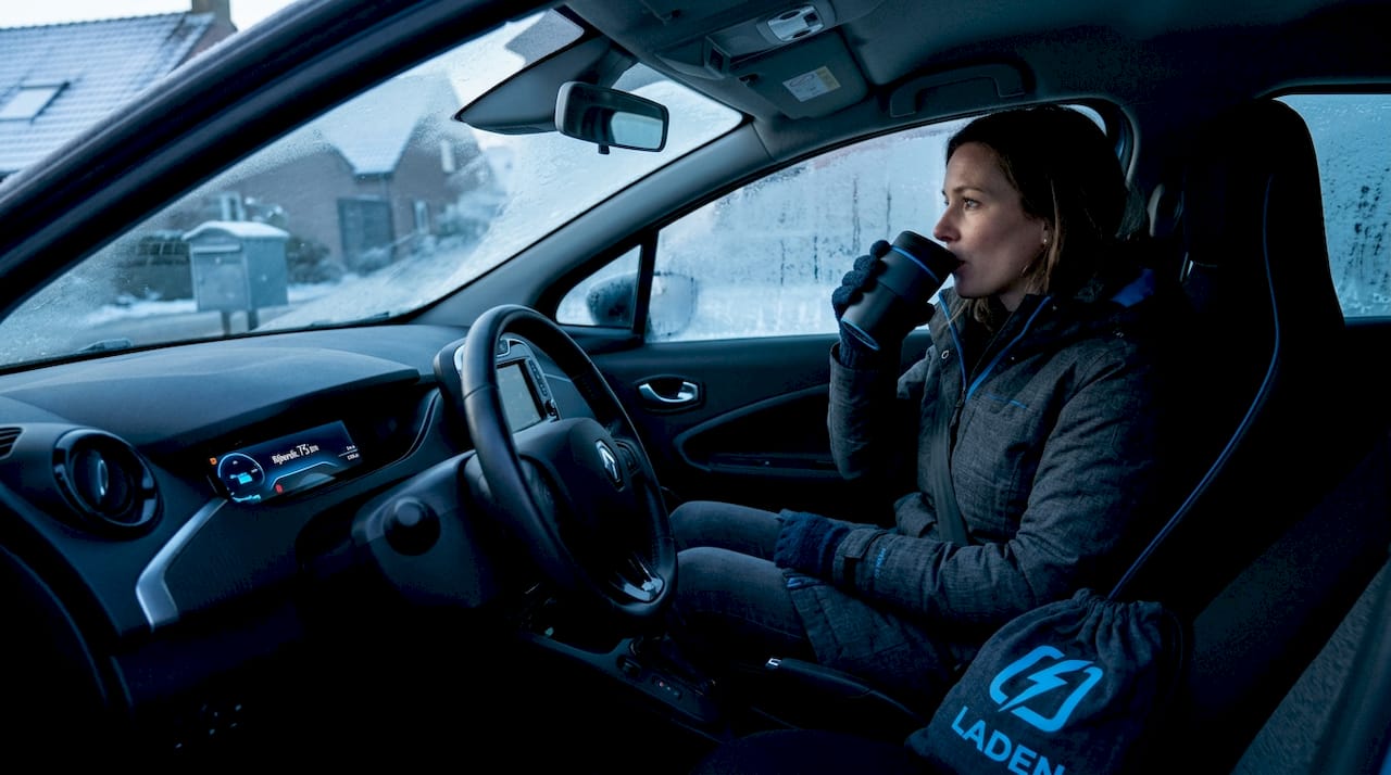 Een vrouw bekijkt in de winter hoeveel kilometers ze nog met haar elektrische auto kan rijden.