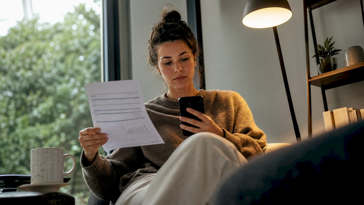 Een vrouw bekijkt haar energierekening terwijl ze bij de warmtepomp staat.