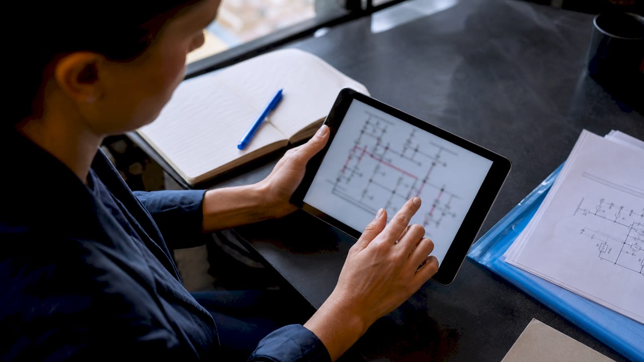 Zoom sur des mains manipulant une tablette affichant le schéma d’un réseau électrique