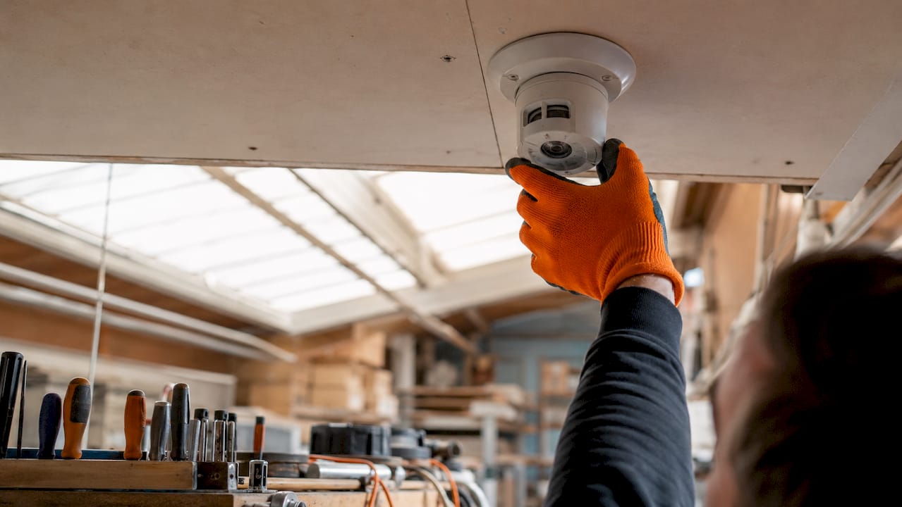 Worker installing flame detector sensor on ceiling