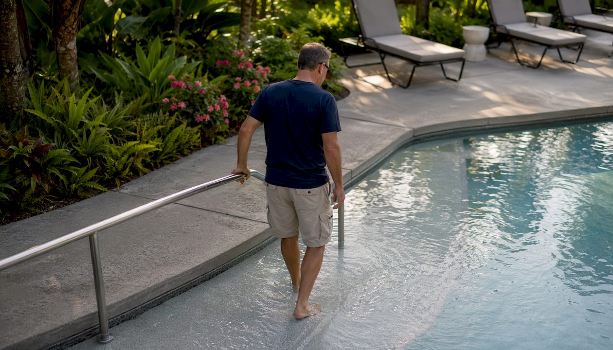 Pool Accessibility Design: ADA Compliance Guide for 2026 2 Man using sloped pool entry with handrail