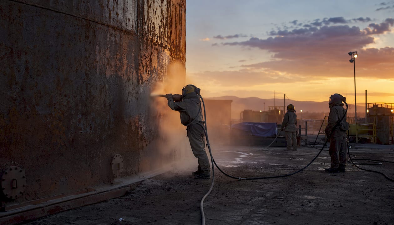 Close-up abrasive particles blasting steel tank surface