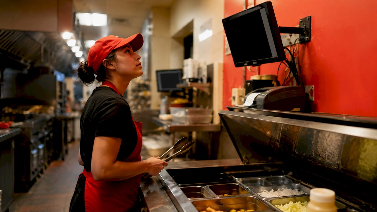 Cook checking kitchen display system in fast food kitchen