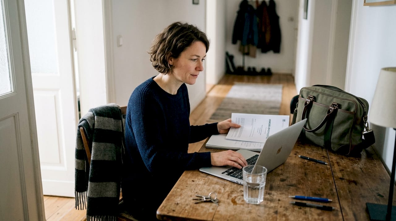 Eine Frau sitzt an einem Holztisch und übergibt das Immobiliengutachten.