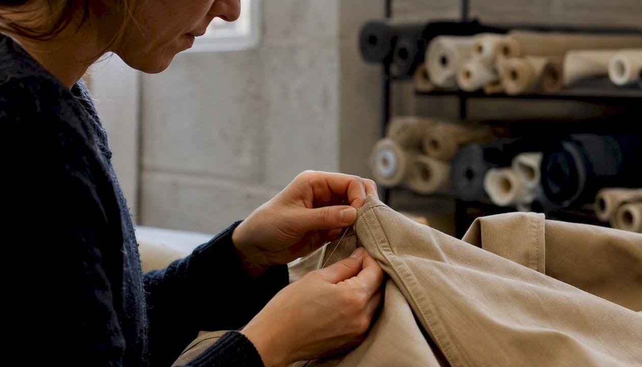 Des mains s’appliquent à renforcer la couture d’un vêtement, assurant solidité et finition soignée.