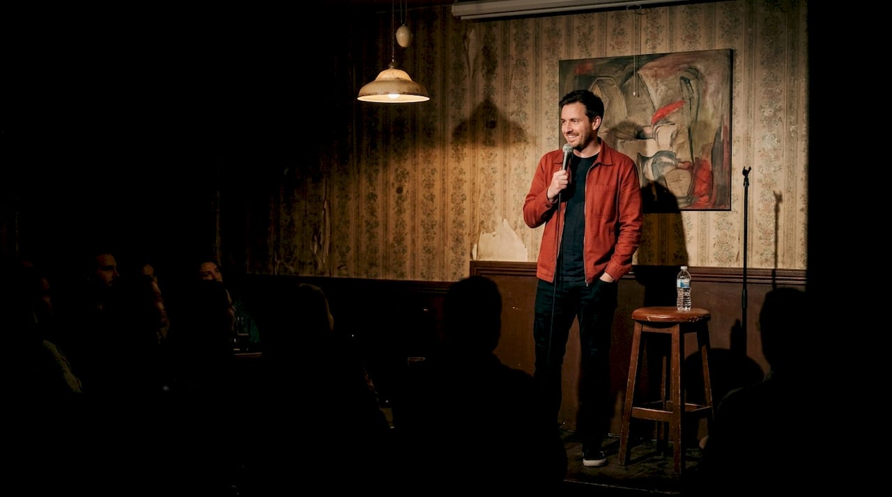 Standupkomiker som kör sitt material inför en liten publik i en mysig källarlokal.