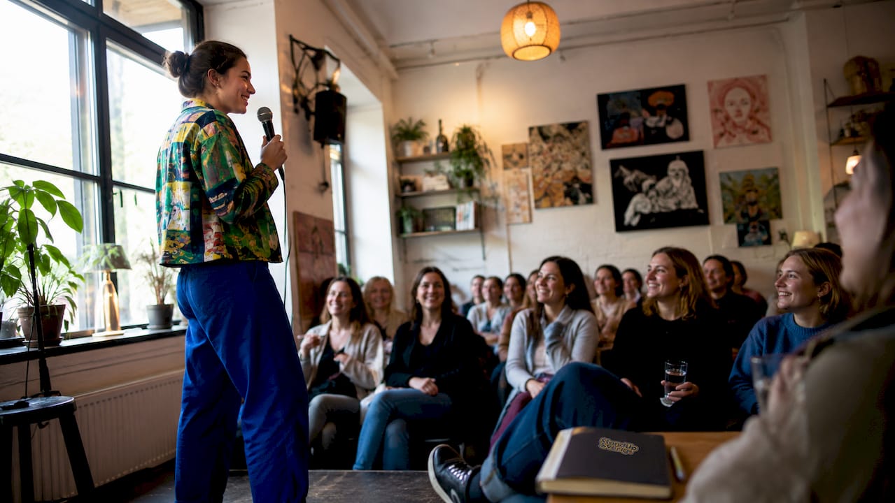 En kvinnlig komiker uppträder med standup på en liten, mysig scen
