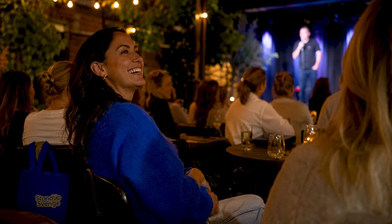 En kvinna i publiken skrattar gott under en standupföreställning.