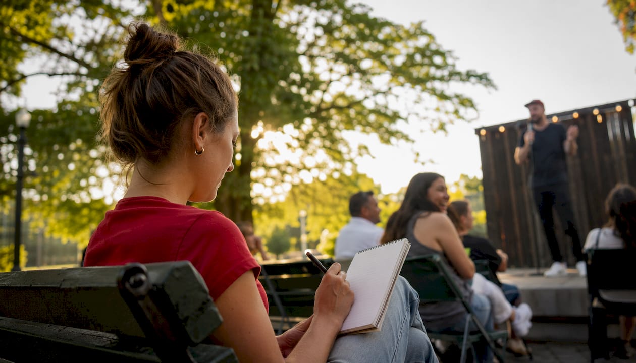 En ung kvinna sitter och gör anteckningar under ett open mic-event.