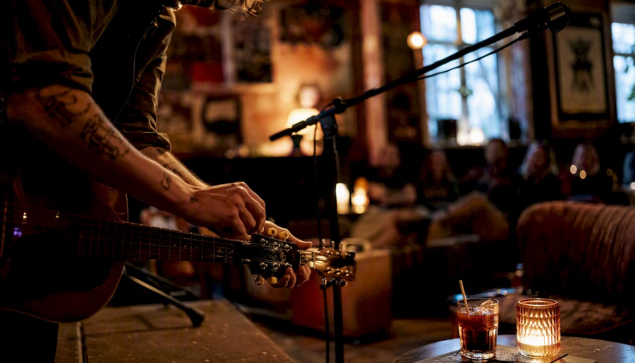 En musiker står på scenen och stämmer sin gitarr i den mysiga baren.