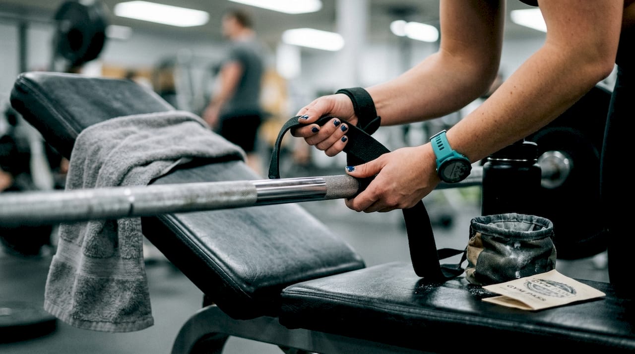 Hands securing lifting straps on gym barbell