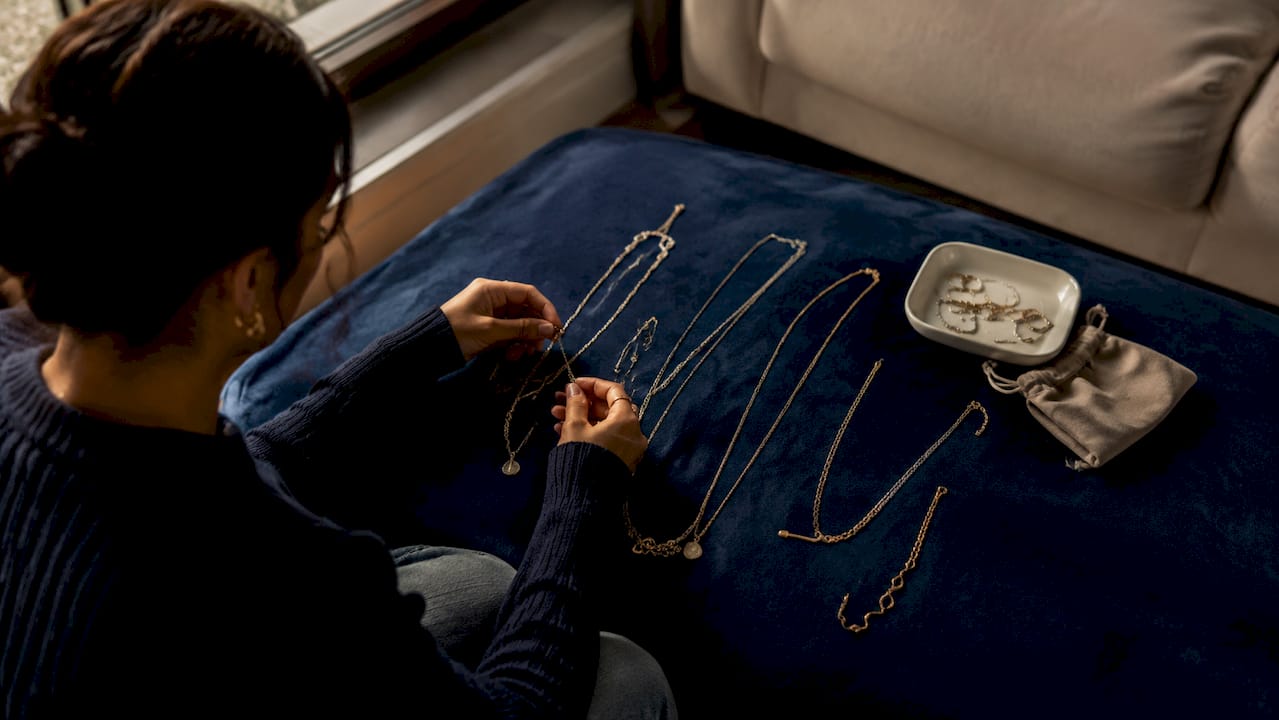 Hands layering layered luxury jewelry on surface