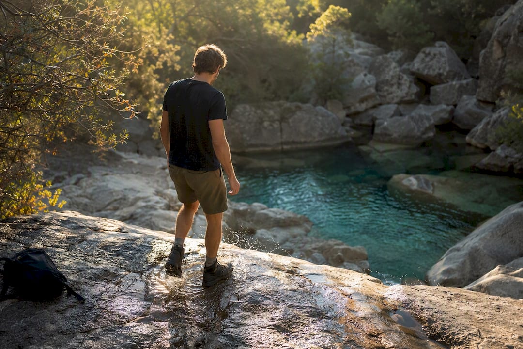 Une paire de chaussures de randonnée et une gourde posées au bord d’un bassin naturel.