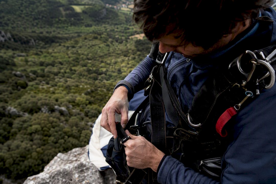 Aux premières lueurs du jour, des mains s’affairent à ajuster le harnais du parachute.