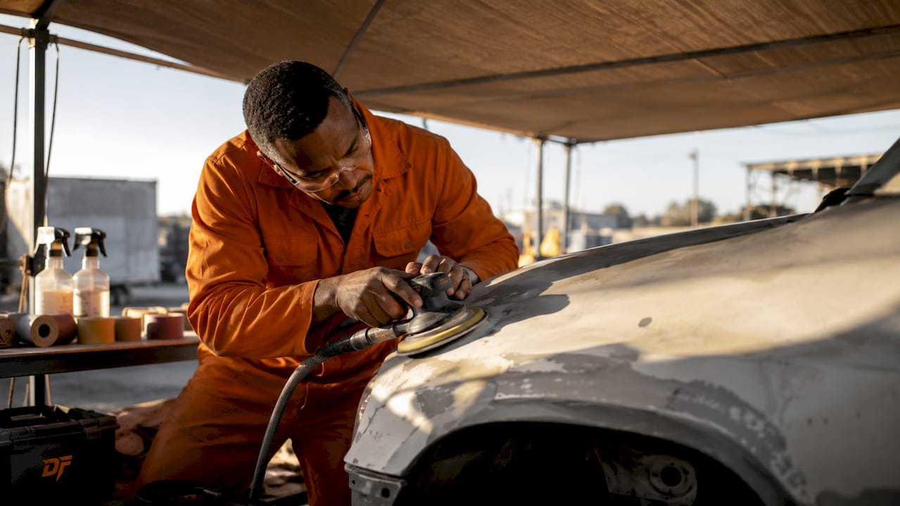 Technician sanding car fender with tools nearby