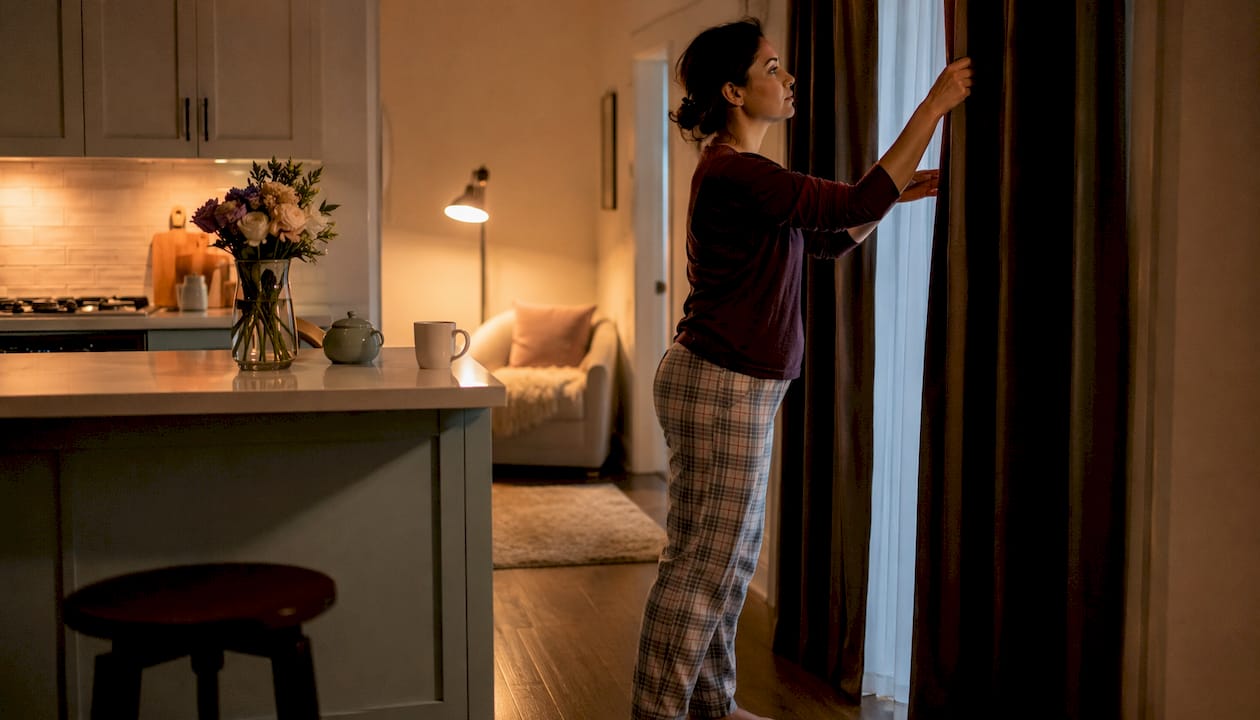 Woman adjusting curtains in bedroom for better sleep