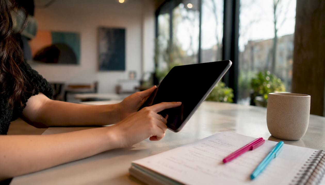 Detailaufnahme: Hände tippen auf einem Tablet im modernen Coworking-Bereich.