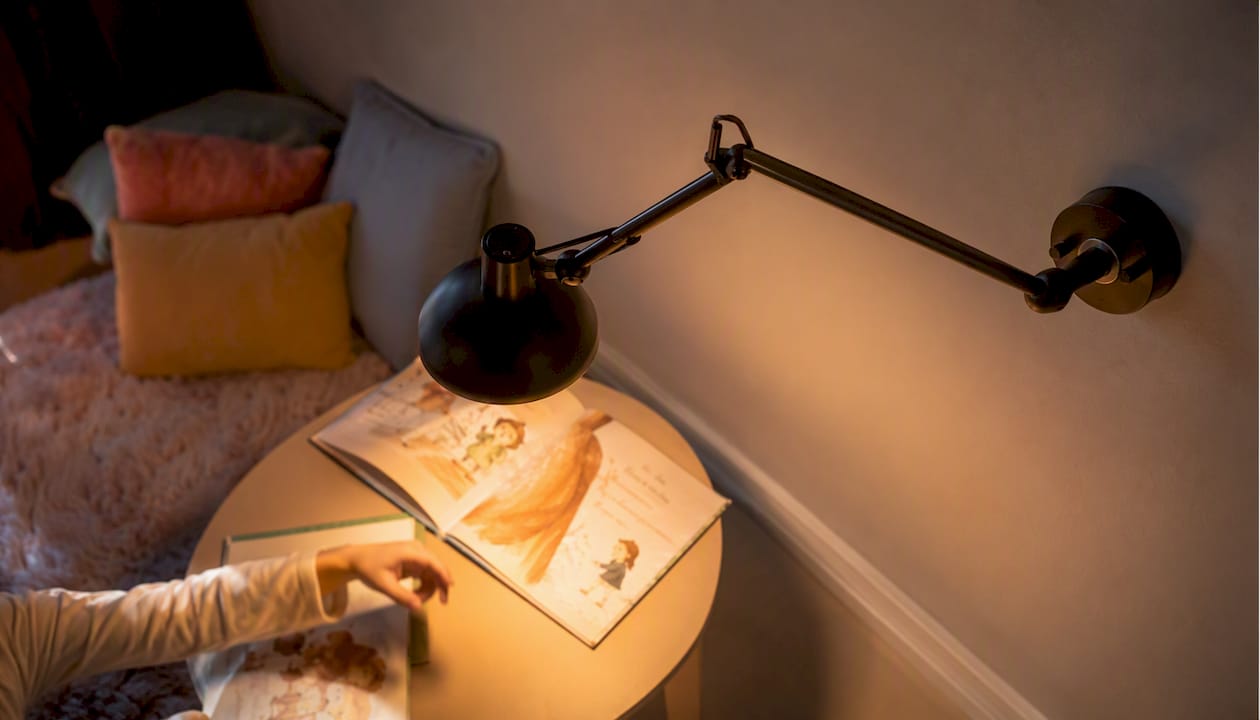 Eine gemütliche Leseecke für Kinder, beleuchtet von einer Wandlampe mit integriertem Leselicht.