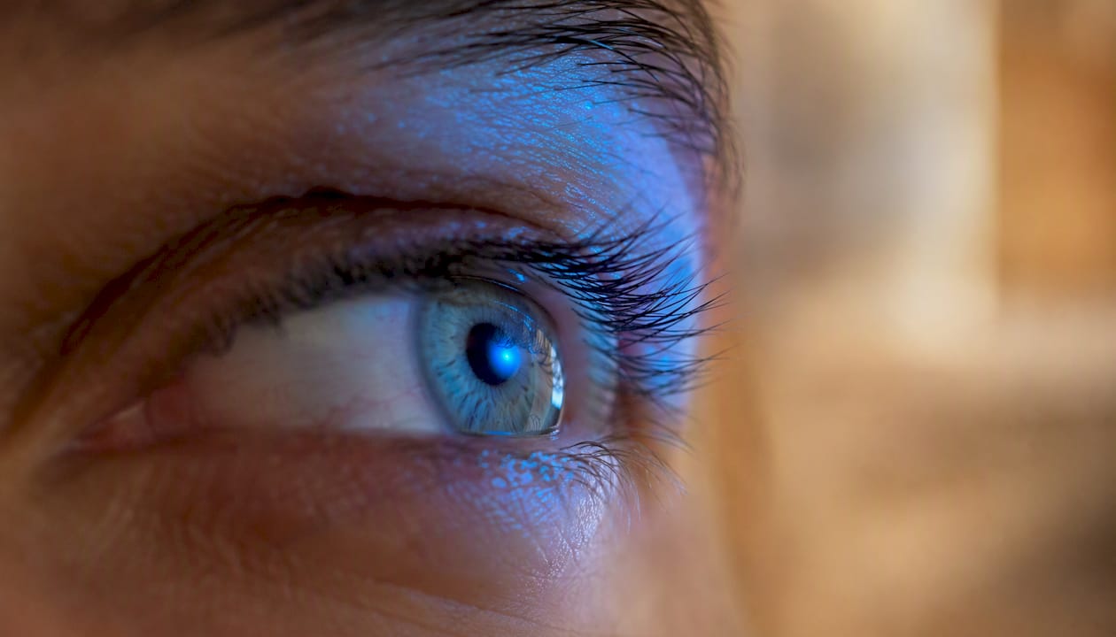 Ein Auge im Fokus, das von blauem Licht eindrucksvoll beleuchtet wird.
