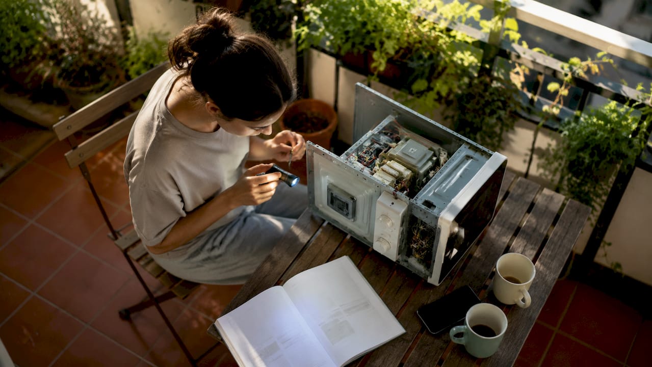 Beneficios de reparar a tiempo tus electrodomésticos 2 Una mujer revisa el microondas averiado en la cocina, tratando de descubrir por qué no funciona.