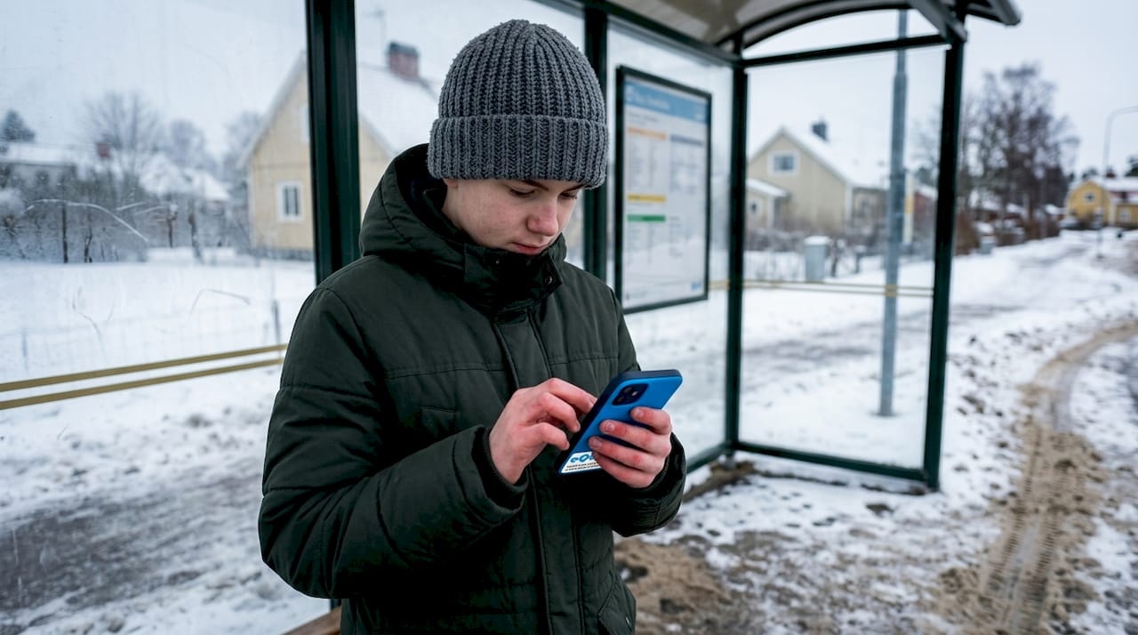 En tonåring står ute i vinterkylan och scrollar på mobilen.