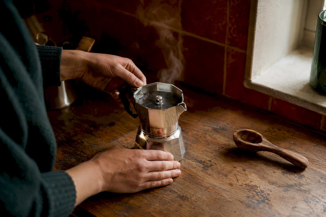 Hands assembling moka pot with steam beginning to escape