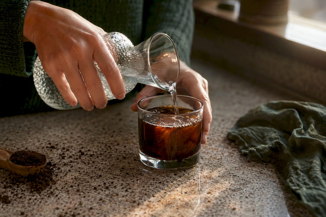 Hands diluting cold brew concentrate with water