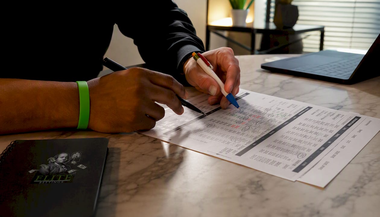 Hands comparing NBA betting lines on paper