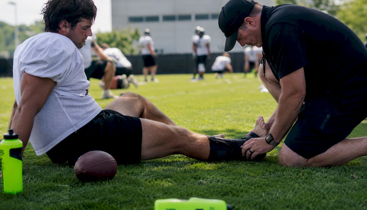Coach inspecting football player's ankle brace