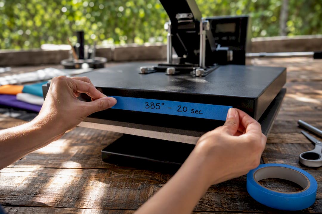 Hands marking heat press settings on painter's tape