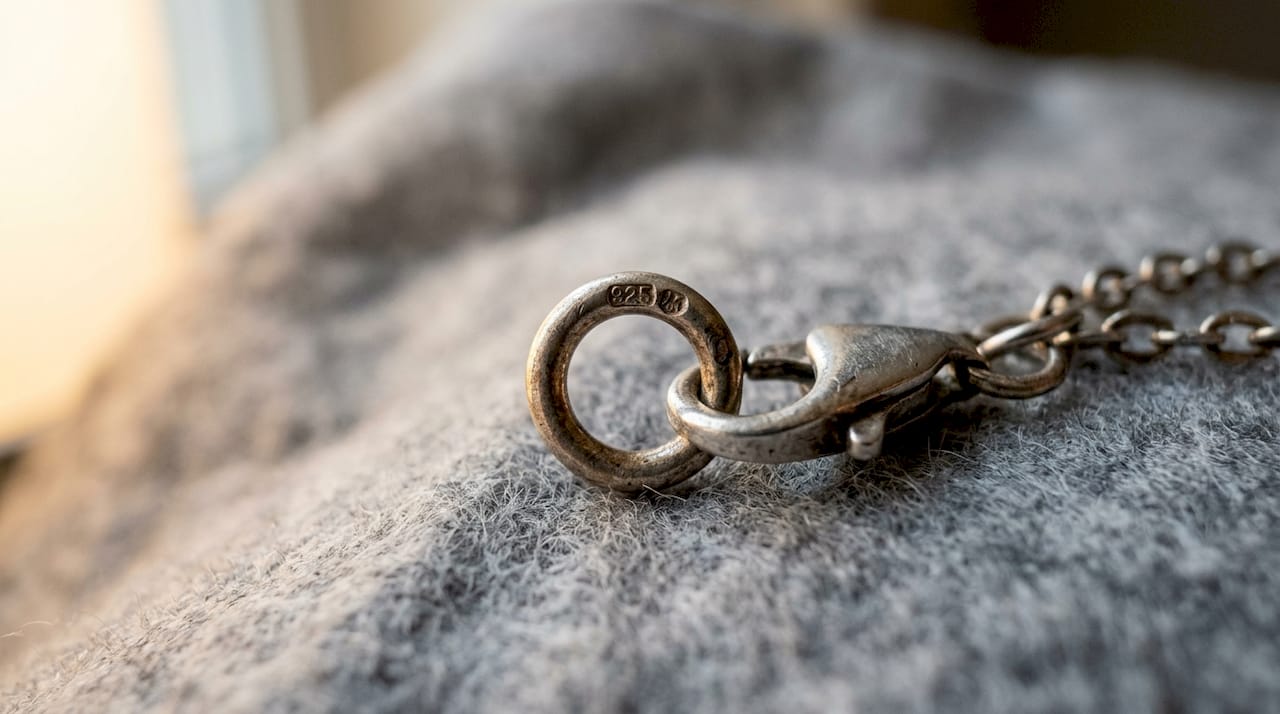 Close-up of silver necklace clasp with hallmark stamp