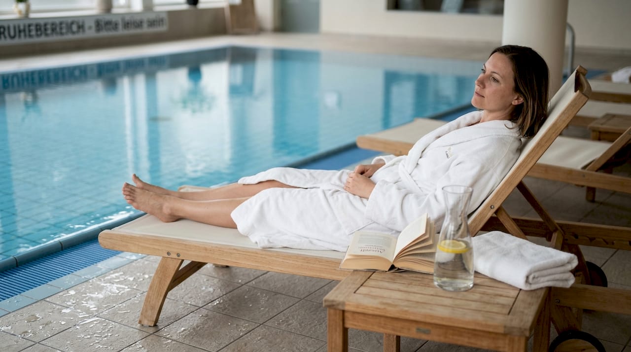 Eine Frau genie&szlig;t entspannte Stunden auf der Liege am Hotelpool im Spa-Bereich.