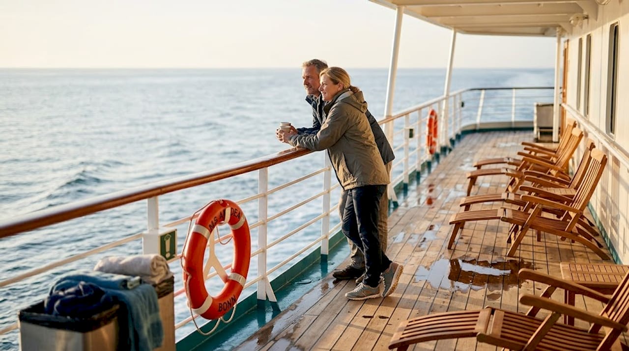 Ein Paar genie&szlig;t am fr&uuml;hen Morgen die frische Meeresluft auf dem Sonnendeck ihres Kreuzfahrtschiffs.