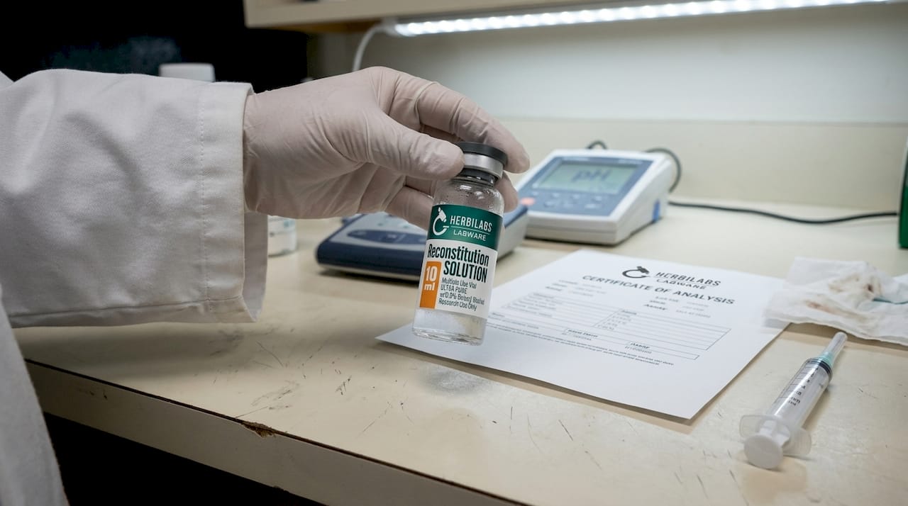 Hand holds bacteriostatic water vial on bench