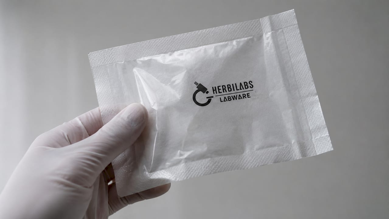 Gros plan sur une main gantée tenant une pochette stérile en papier-plastique.