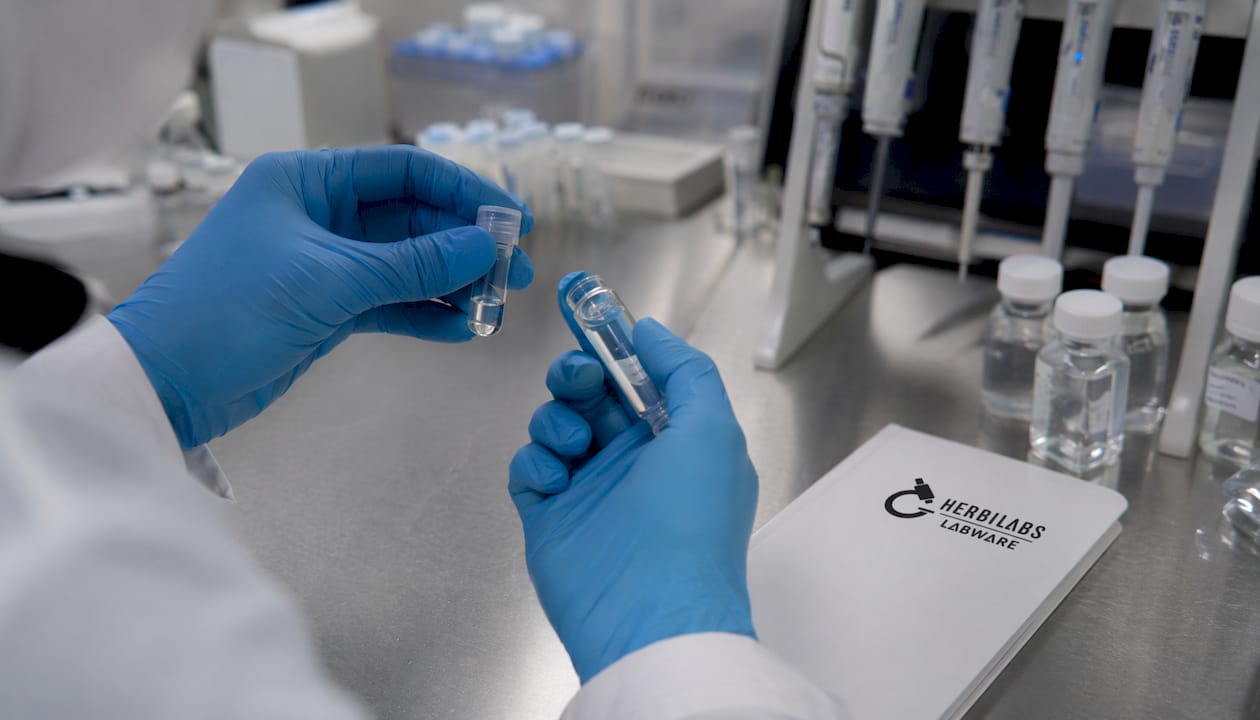 Des mains protégées par des gants manipulent délicatement des flacons contenant des peptides.