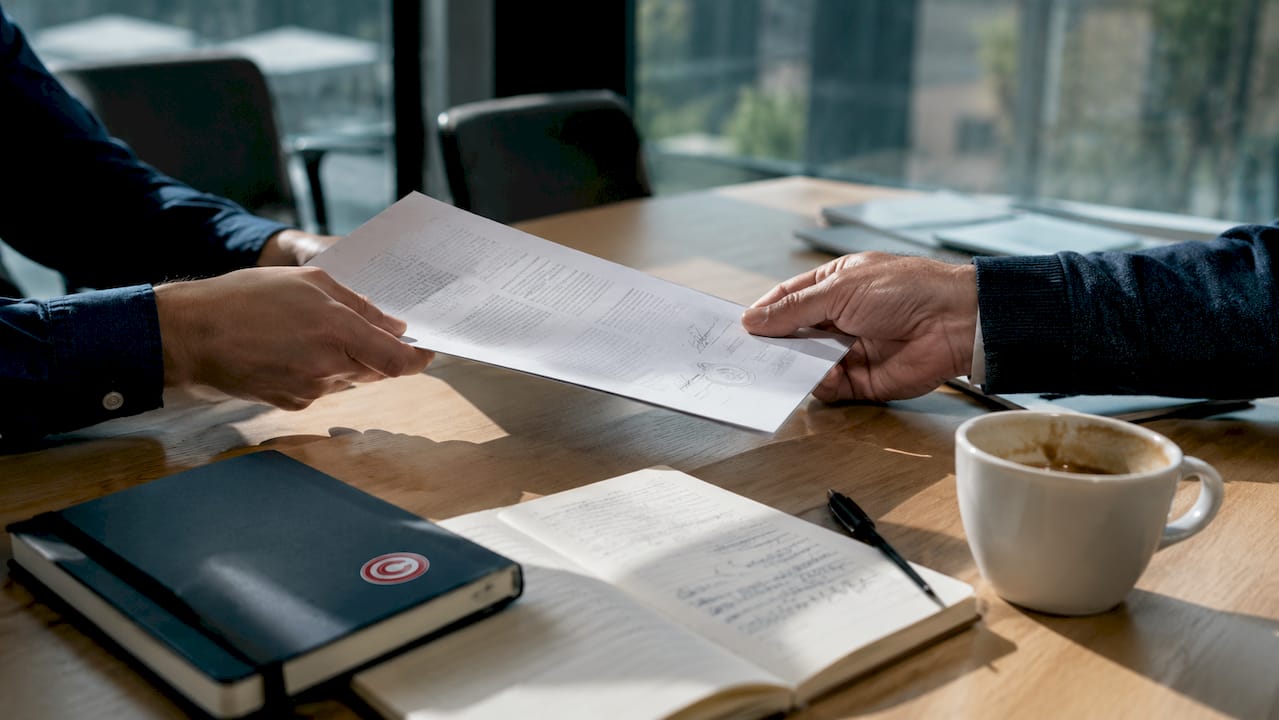 Due persone si passano i documenti di un contratto, a suggellare un accordo.
