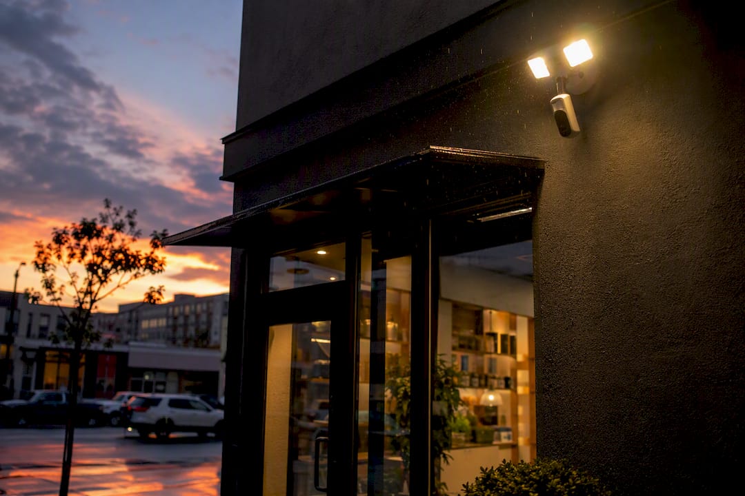Floodlight and security camera over storefront entrance at dusk