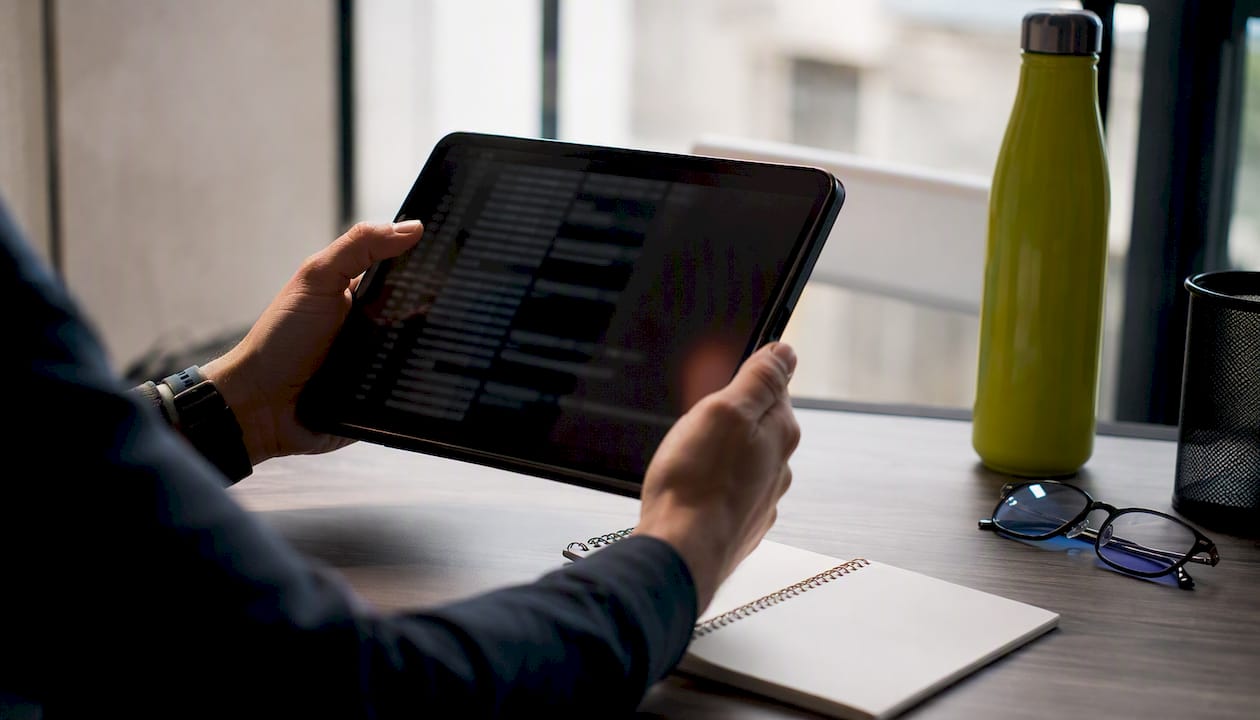 Hands reviewing server logs and tablet with dark screen