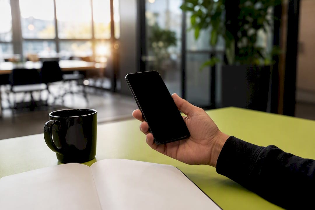 Hand holding smartphone on desk with coffee cup