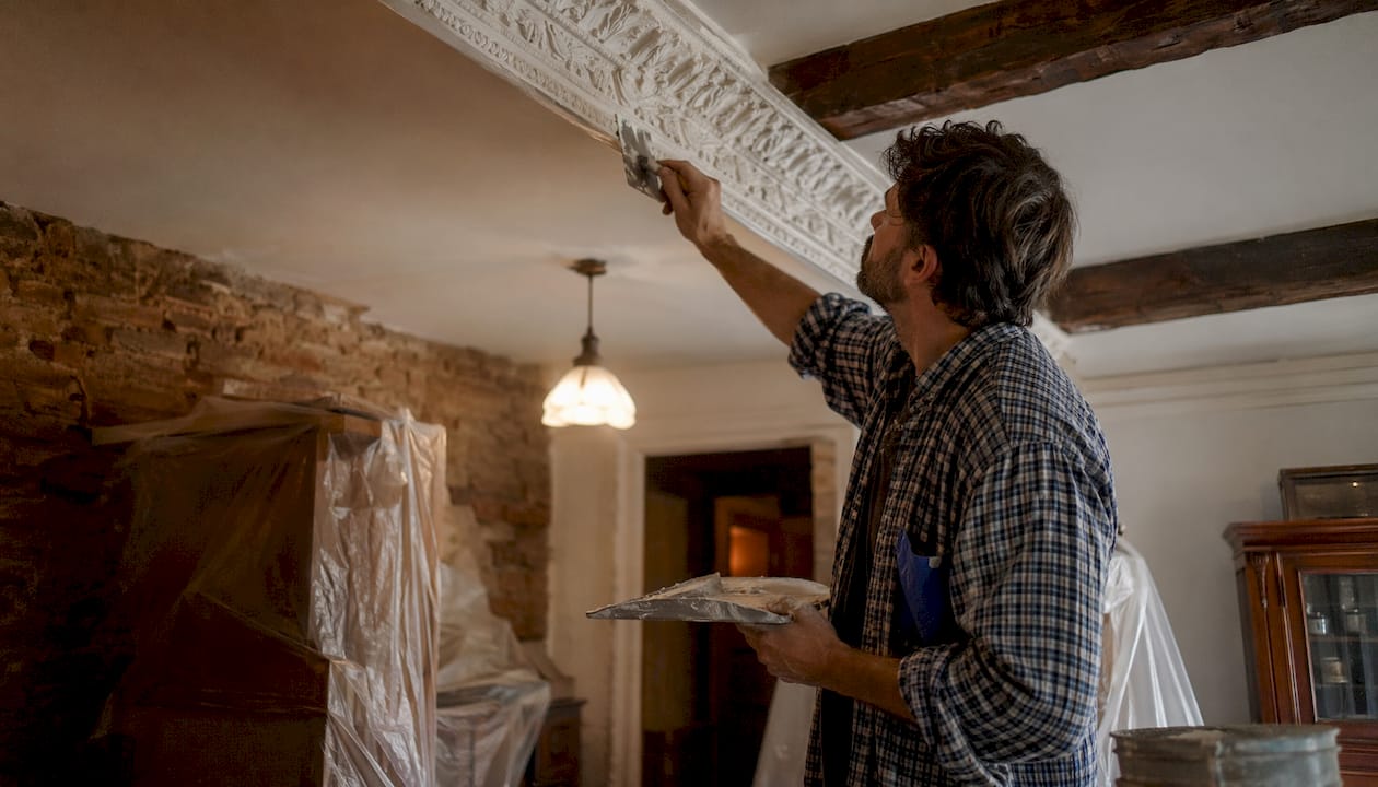 Hands applying lime plaster on cornice moulding